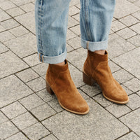 Brown ankle boots worn with rolled-up jeans on a paved surface