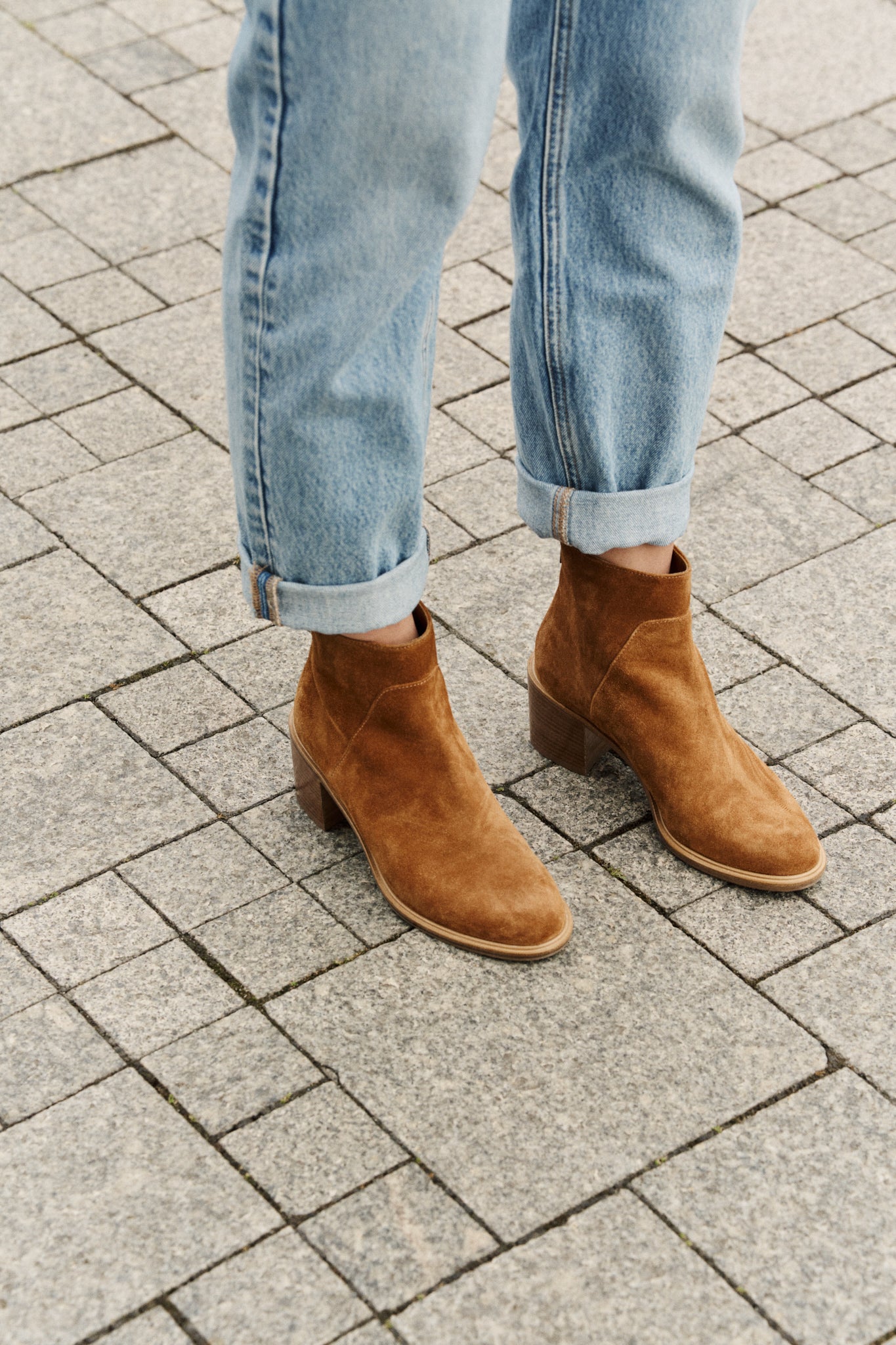 Brown ankle boots worn with rolled-up jeans on a paved surface
